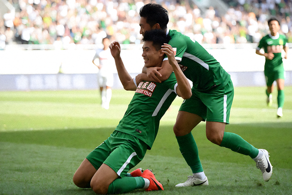 足球球员进球后滑跪庆祝，队友从后方跑来拥抱